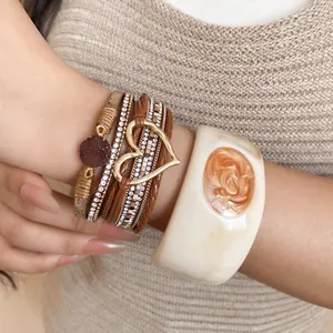 Close-up detail of multi-layer leather bracelet with rhinestone heart and resin bangle.