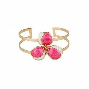 Elegant gold-toned open cuff bracelet featuring a pink and white enamel flower design