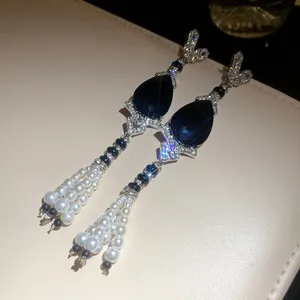 Macro view of teardrop dark blue stone earrings featuring elegant multi-strand pearl tassels