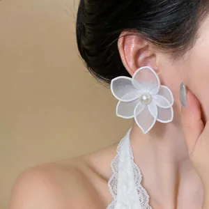 Close-up of white silk mesh flower earring with pearl on model's ear