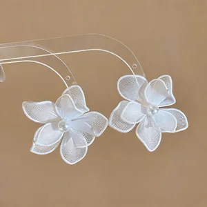 Detailed macro shot of white mesh floral earrings featuring central pearl on clear stand