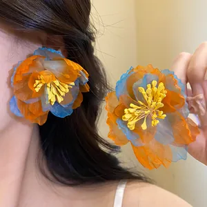 Detail shot of oversized orange and blue chiffon flower earrings with yellow centers.