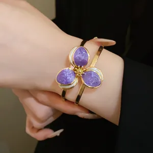Exquisite detail view of a vintage gold bangle featuring purple enamel flower petals on a hand