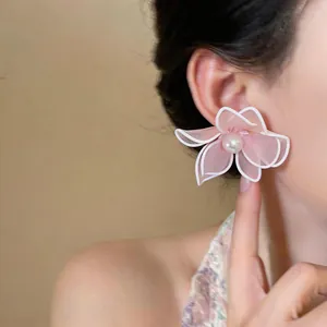 Detailed close-up view of a pink mesh flower stud earring with a central pearl on a model's ear