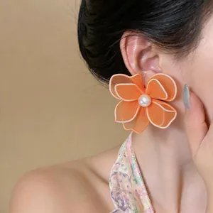 Detailed close-up of orange mesh flower stud earring with pearl center on model's ear