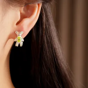 Close-up detail of a cute silver bear stud earring featuring green zircon stones on an ear