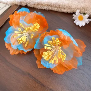 Close-up of vibrant orange and blue chiffon flower earrings with yellow stamens.