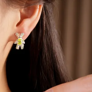 Detailed side view of a cute silver bear stud earring with a green zircon gem on an ear.