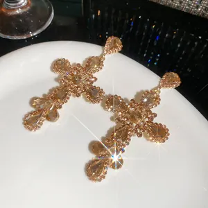 Detailed close-up of sparkling amber crystal cross earrings in vintage gold finish.