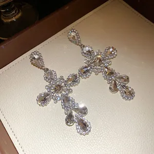 Close-up of sparkling rhinestone cross-shaped drop earrings on cream jewelry tray