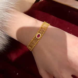 Detail view of a vintage gold-tone hollow bracelet with a red gemstone on a wrist.