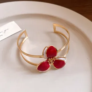 Detailed close-up view of a vintage gold open cuff bracelet with a vibrant red enamel flower