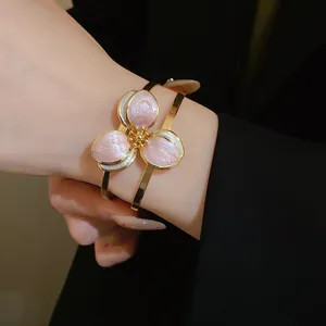 Detail view of a vintage-style gold-toned open bangle with a pink enamel flower.