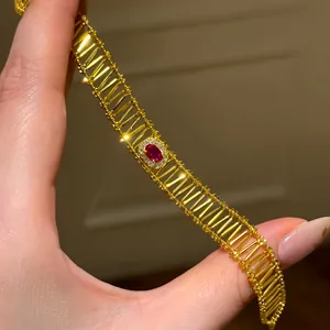 Detail of a vintage gold hollow bracelet with a central oval red gemstone.