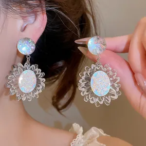 Dettaglio macro di orecchini a margherita trasparenti con centri iridescenti e petali.