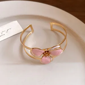 Elegant gold cuff bracelet with pink enamel flower petals and vintage design.