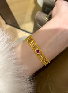 Close-up of a gold hollow bracelet featuring a central red oval zircon gemstone