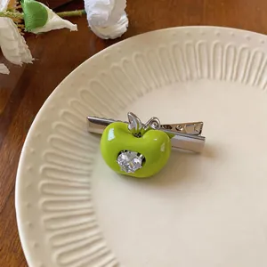 Détail d'une pince à cheveux pomme verte en résine avec un zircon en forme de cœur.