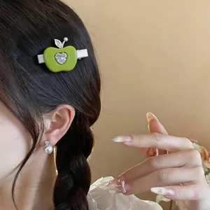 Détail d'une pince à cheveux pomme verte en résine avec un zircon cœur sur le modèle.