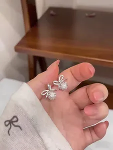 Close-up of hand holding elegant silver bow earrings featuring sparkling round zircon stones