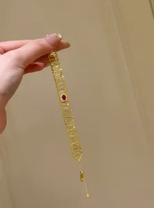 Close-up view of a hand holding a hollow gold bracelet featuring a central red zircon stone