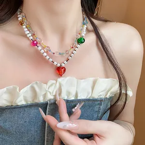 Gros plan d'un collier double rang avec perles blanches et pendentif cœur rouge sur mannequin.