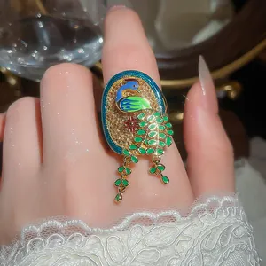 Detailed close-up of an 18K gold-plated peacock ring with vibrant green enamel tassels