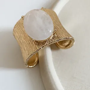 Detail of a gold wrinkled metal cuff bracelet featuring a large oval white stone centerpiece.