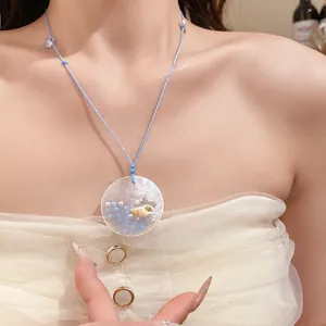 Close-up detail of seashell and blue beads pendant on a woven rope beach necklace.