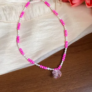 Détail d'un collier de perles roses avec un pendentif en forme de cœur transparent