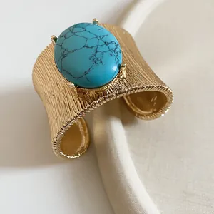Detailed view of textured gold cuff bracelet with large oval turquoise stone.