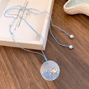 Close-up of a beach-style blue cord necklace with shell and pearl pendant details.