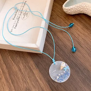 Detail view of coastal blue cord necklace featuring a round seashell and pearl pendant