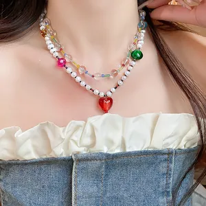 Gros plan d'un collier à deux rangs avec perles et pendentif cœur en verre rouge.