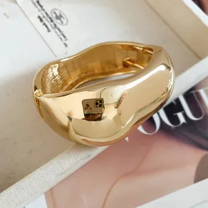 Close-up detail of a gold-plated wavy crumpled metal cuff bracelet with mirror finish