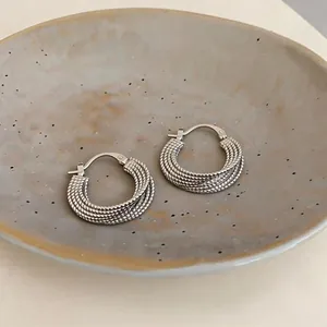 Dettaglio di orecchini a cerchio in argento testurizzato in una ciotola di ceramica.