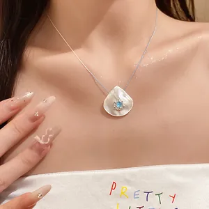 Detail view of a shell pendant necklace with a blue gemstone on a woman's neckline