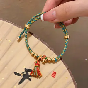 Detailaufnahme eines bunten geflochtenen Seilarmbands mit goldenem Baum-Anhänger und Quaste.