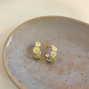 Close-up of C-shaped earrings with yellow enamel flower design on ceramic plate