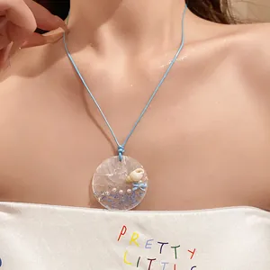 Close-up of dopamine shell and pearl pendant necklace on a light blue cord.