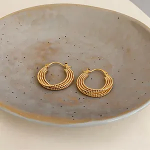 Primo piano di orecchini a cerchio placcati oro 18k con design testurizzato a più fili.