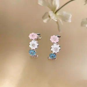 Macro view of C-shaped earrings featuring pink, white, and blue enamel flowers with zircons.