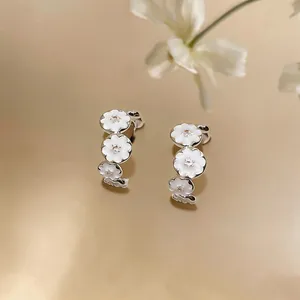 Detail view of elegant C-shaped earrings with white enamel flowers and zircon centers.