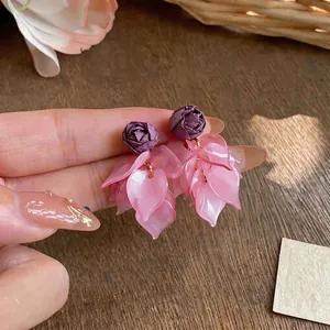 Hand holding elegant purple fabric rose and pink acrylic petal tassel earrings
