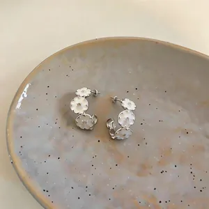 Macro view showing the fine details of silver-tone C-hoop earrings with white enamel flowers