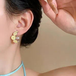 Detail view of sweet C-shaped hoop earrings with yellow oil-dripped flowers and zircons.