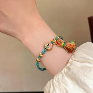 Detailansicht eines geflochtenen türkisblauen Kordelarmbands mit Goldperlen und Quaste.