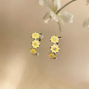 Detail view of C-shaped earrings with yellow enamel flowers and sparkling zircon center.