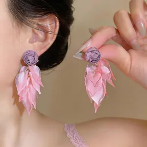 Close-up of pink acrylic petal tassel earrings with a purple fabric rose stud.