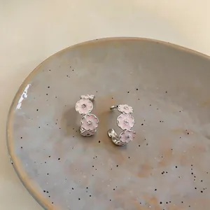 Close-up of pink enamel flower C-shaped earrings with zircon accents on a ceramic plate